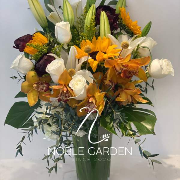 Mixed bouquet of lilies, roses, orchids, and sunflowers in a glass vase