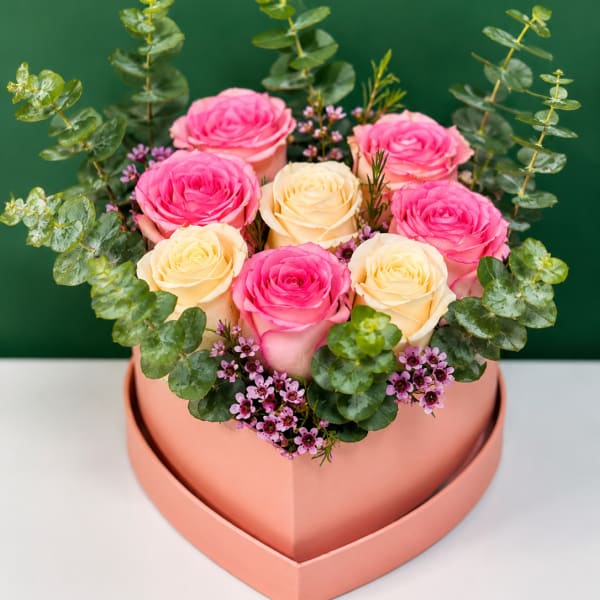 Pink and cream roses arranged in a heart-shaped box