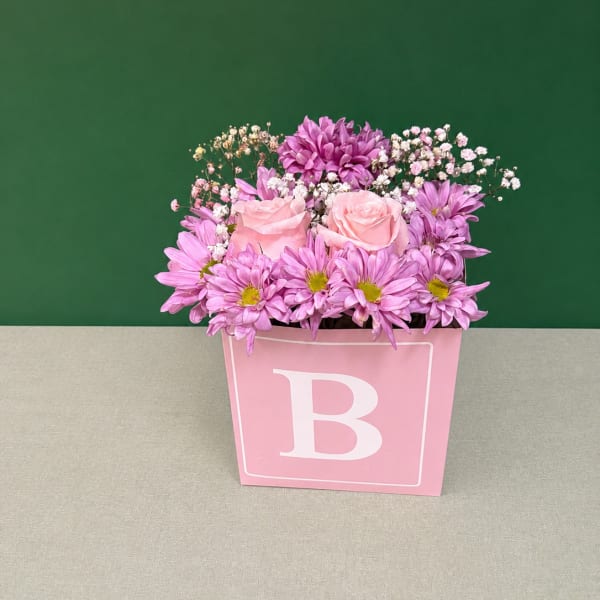 Pink and purple flowers arranged in a pink box with a large letter B
