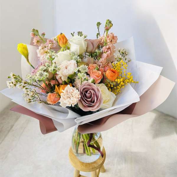 Mixed pastel bouquet in a glass vase on a small stool