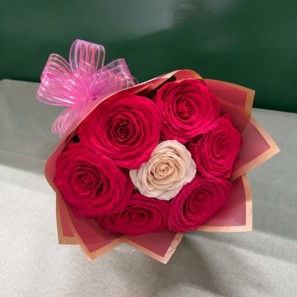 Bouquet of hot pink and cream roses wrapped in pink paper with a ribbon bow