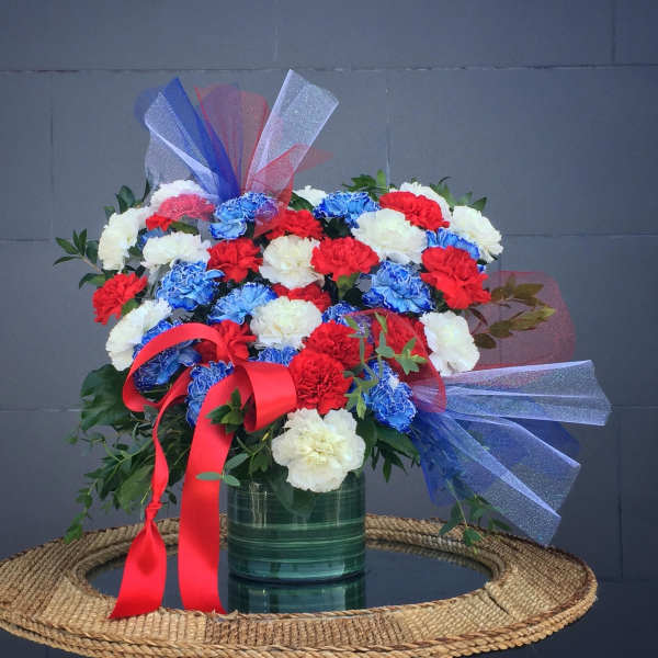 Bouquet of red, white, and blue carnations in a green vase with ribbon bows
