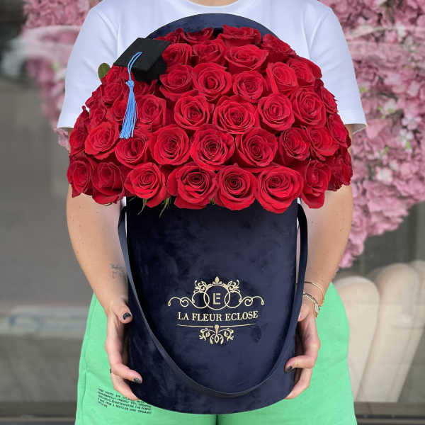 Large bouquet of red roses in a navy hatbox with a graduation cap topper