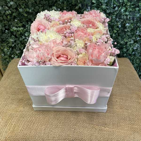 Pink and white roses arranged in a white box with a pink ribbon