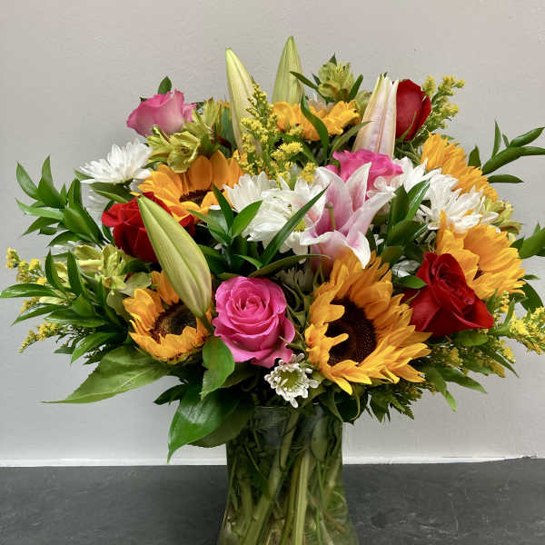 Mixed bouquet of sunflowers, roses, lilies, and daisies in a glass vase