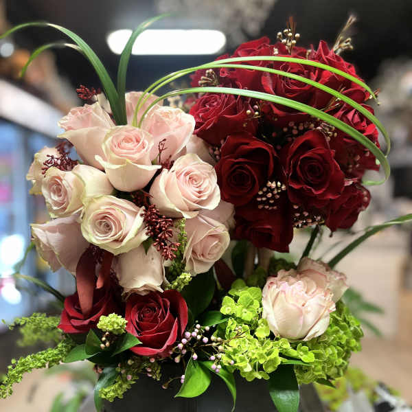 Red and pale pink roses arranged in a black vase with green accents.