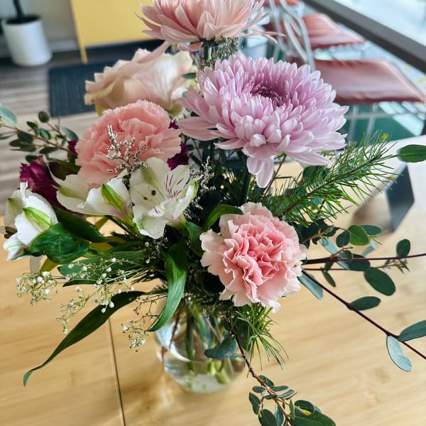 Vase arrangement of pink chrysanthemums, carnations, and white blooms on a wooden table