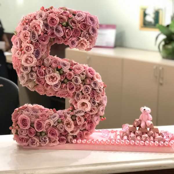 Pink rose letter display with a small teddy bear and chocolates