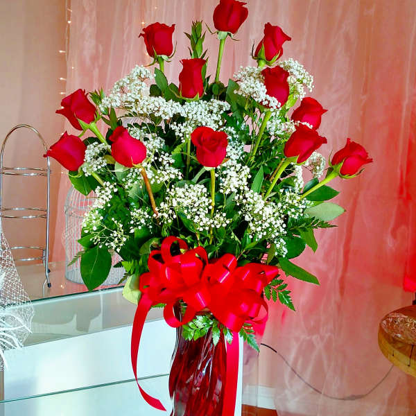 Red roses arranged in a red glass vase with a large ribbon bow