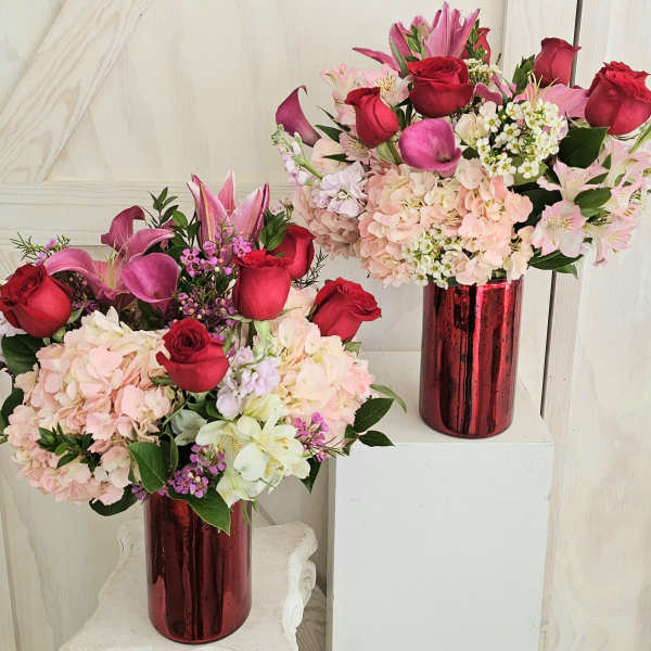 Two bouquets of red roses, pink lilies, and pale hydrangeas in red vases