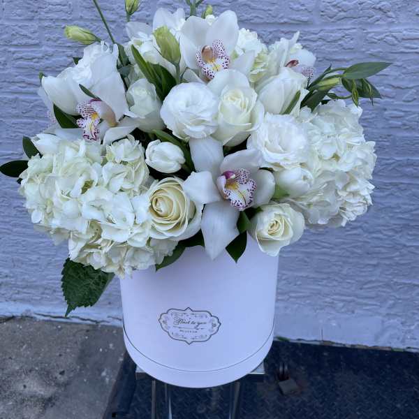 White floral arrangement in a round white box with orchids and roses