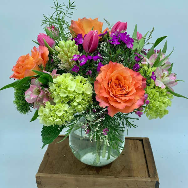 Mixed bouquet of orange roses, pink tulips, and green hydrangeas in a glass vase