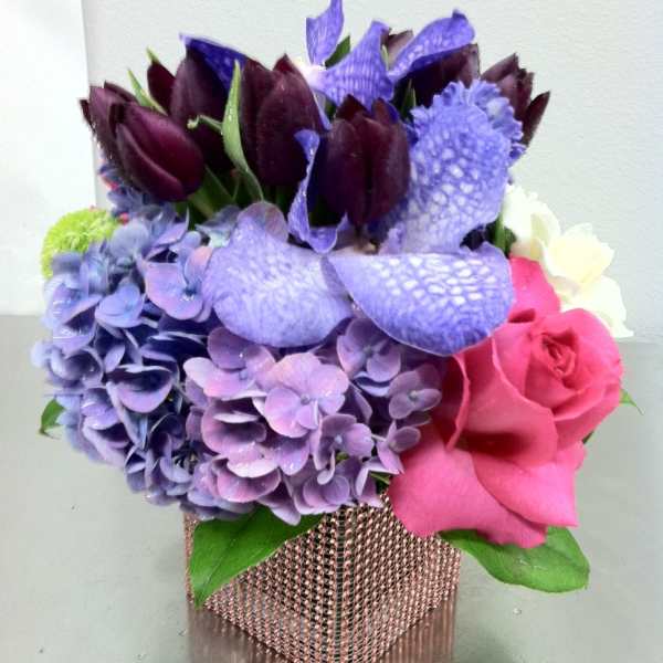 Bouquet of purple hydrangeas, dark tulips, pink roses, and calla lilies in a square vase