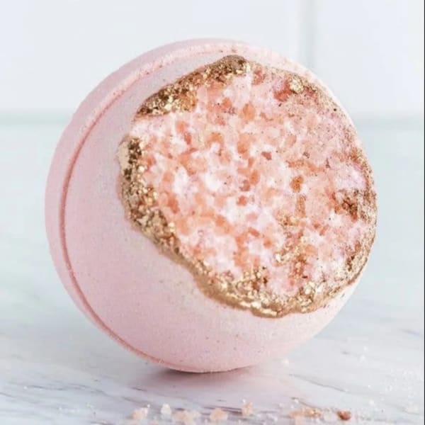 Pink bath bomb with gold and peach glitter on a marble surface