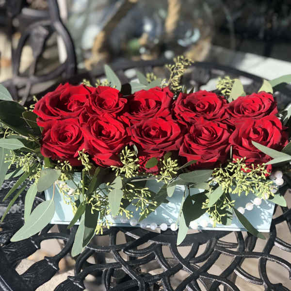 Red roses arranged in a low rectangular box with greenery