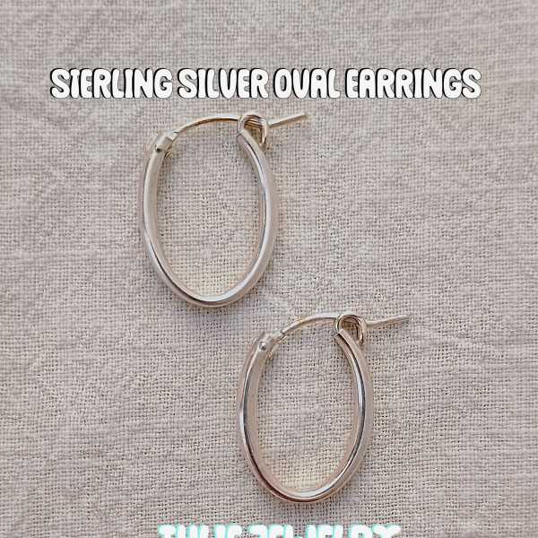 Pair of silver oval hoop earrings on a textured fabric background