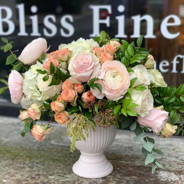 Blush and cream floral arrangement in a white pedestal vase