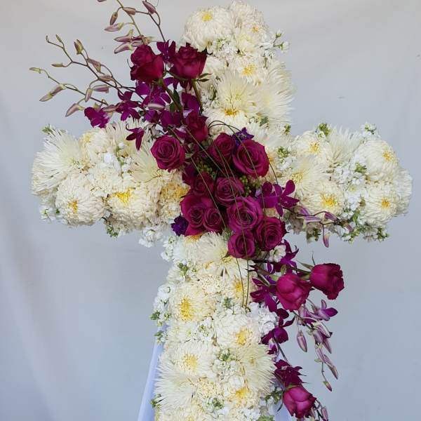 Cross-shaped floral arrangement of white chrysanthemums and magenta roses on a stand