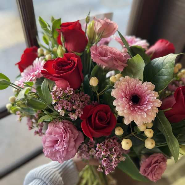 Bouquet of red and pink roses with pink daisies in a hand-held wrap