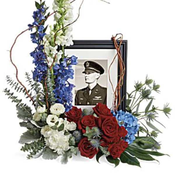 Floral tribute around a framed military portrait with red, white, and blue flowers