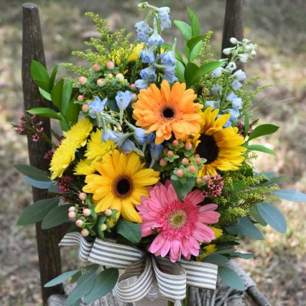 Mixed bouquet with gerbera daisies, sunflowers, and blue flowers in a glass vase