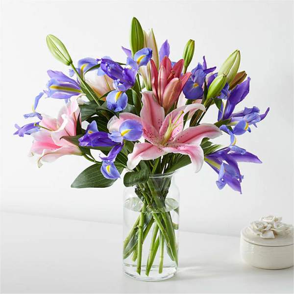 Bouquet of pink lilies and purple irises in a clear glass vase