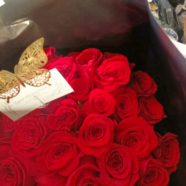 Bouquet of red roses wrapped in dark paper with a butterfly tag