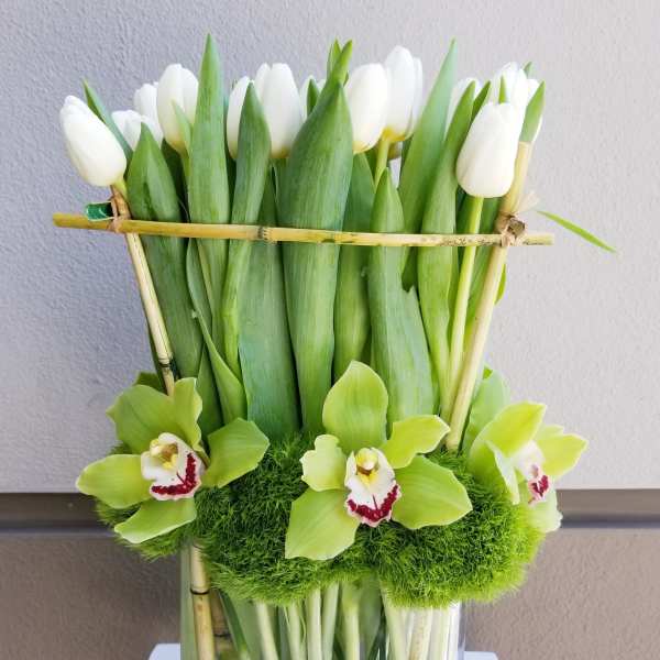 White tulips and green orchids in a glass vase with bamboo accents