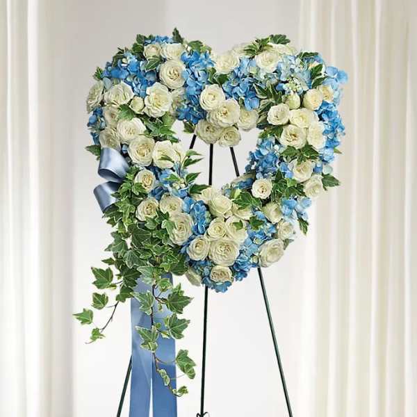 Heart-shaped floral wreath of white and blue flowers on a stand with a blue ribbon