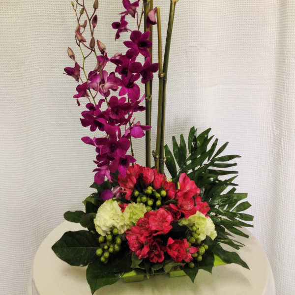 Tall floral arrangement with purple orchids and pink blooms in a low container