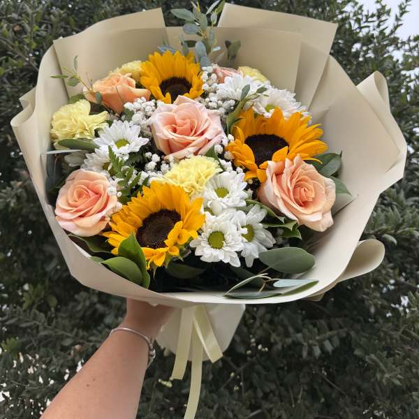 Bouquet of peach roses, sunflowers, and white daisies in beige wrap