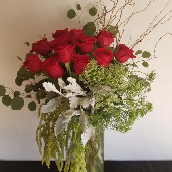 Red roses in a glass vase with green filler and silver foliage