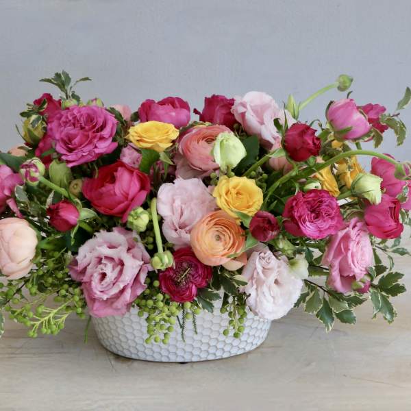 Low centerpiece of bright pink, yellow, and peach blooms in a white ceramic bowl.