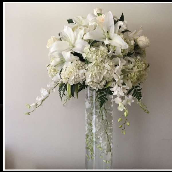 White floral arrangement with lilies and hydrangeas in a tall clear vase