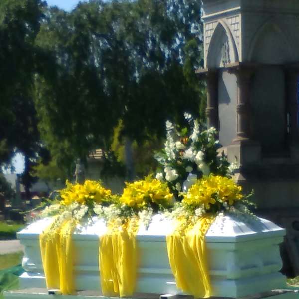 White casket with yellow floral sprays and draped yellow fabric outdoors