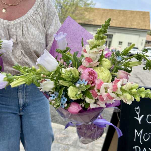 Handheld bouquet of pink, white, and green flowers wrapped in purple paper