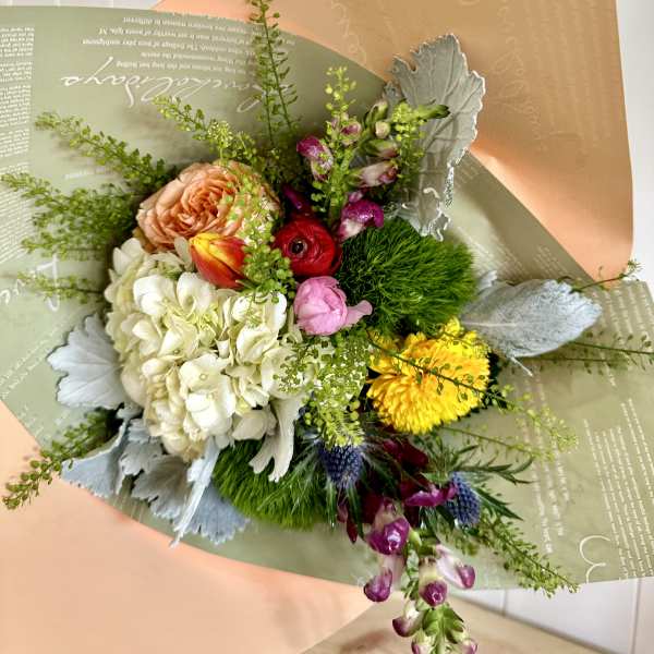 Mixed bouquet with roses, hydrangea, tulips, and yellow blooms in pastel wrapping