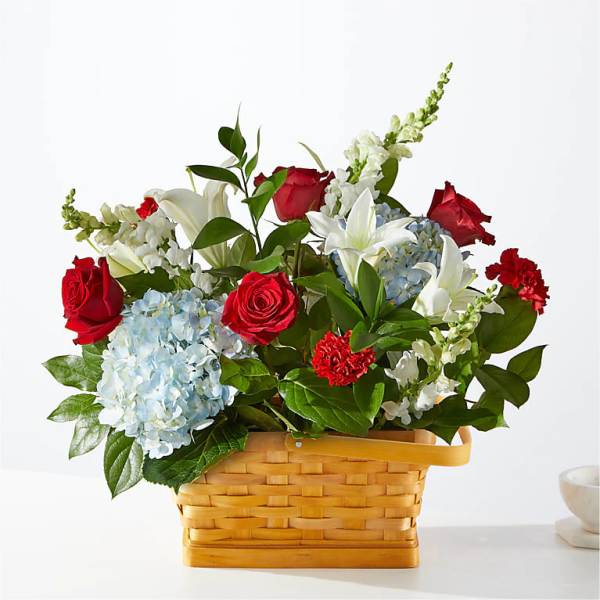 Basket arrangement of red roses, white lilies, and blue hydrangeas