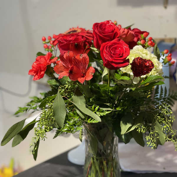 Red roses and mixed red flowers in a clear glass vase