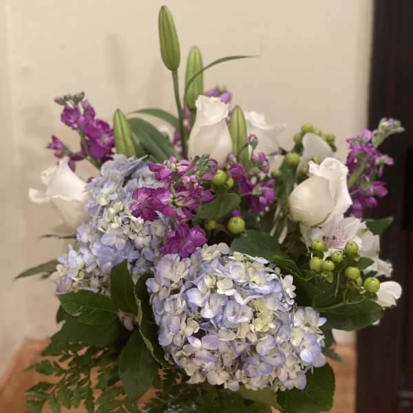 Bouquet of blue hydrangeas, white roses, and purple flowers in a glass vase