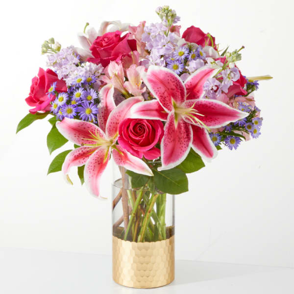 Pink lilies and roses in a clear vase with a gold base