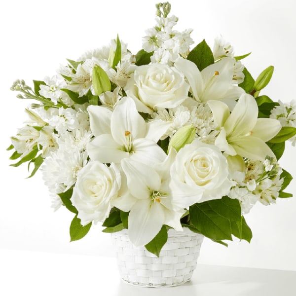 White lilies and roses arranged in a white basket vase