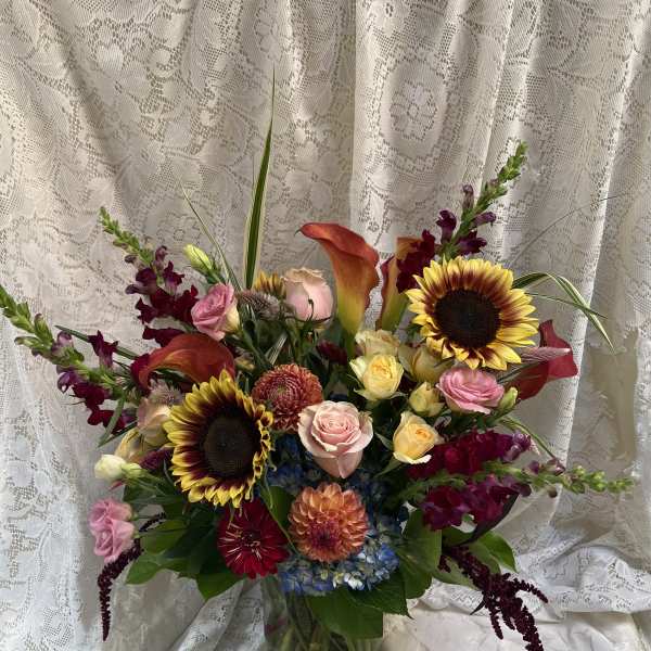 Mixed bouquet with sunflowers, roses, calla lilies, and orchids in a glass vase