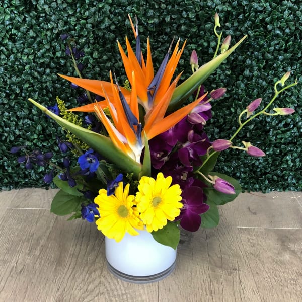 Tropical bouquet with orange bird of paradise and purple orchids in a white vase