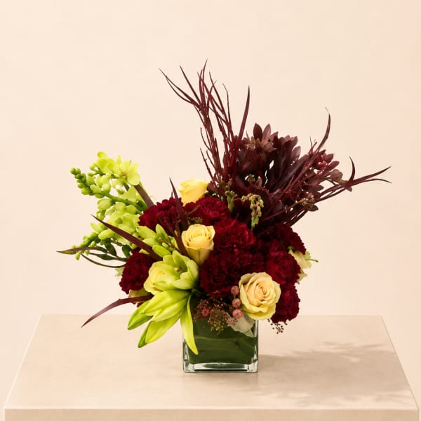 Bouquet of red carnations, yellow roses, and green orchids in a square glass vase