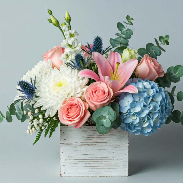 Pink roses, white blooms, blue hydrangea, and lilies in a white wooden box