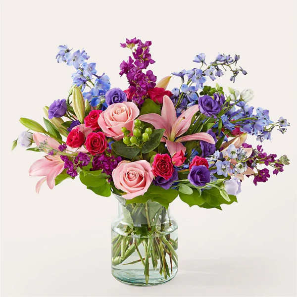 Mixed bouquet of pink, purple, and blue flowers in a glass vase