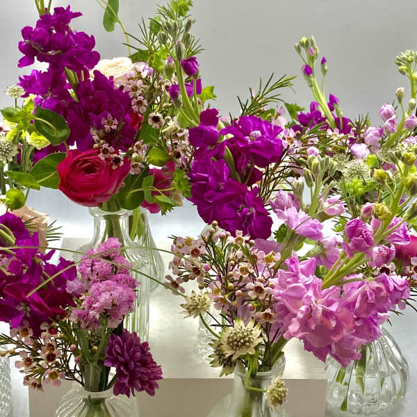 Assorted pink and purple flower arrangements in small glass vases