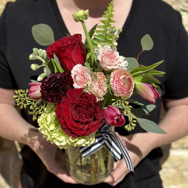 Bouquet of red and pink flowers in a glass vase with a striped ribbon