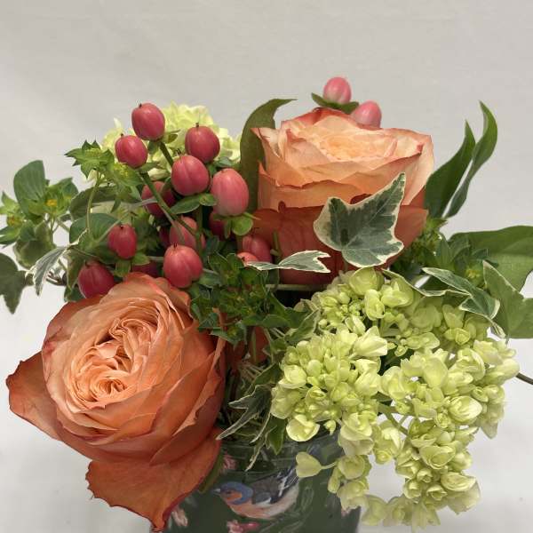 Peach roses with pink berries and pale green hydrangeas in a patterned vase